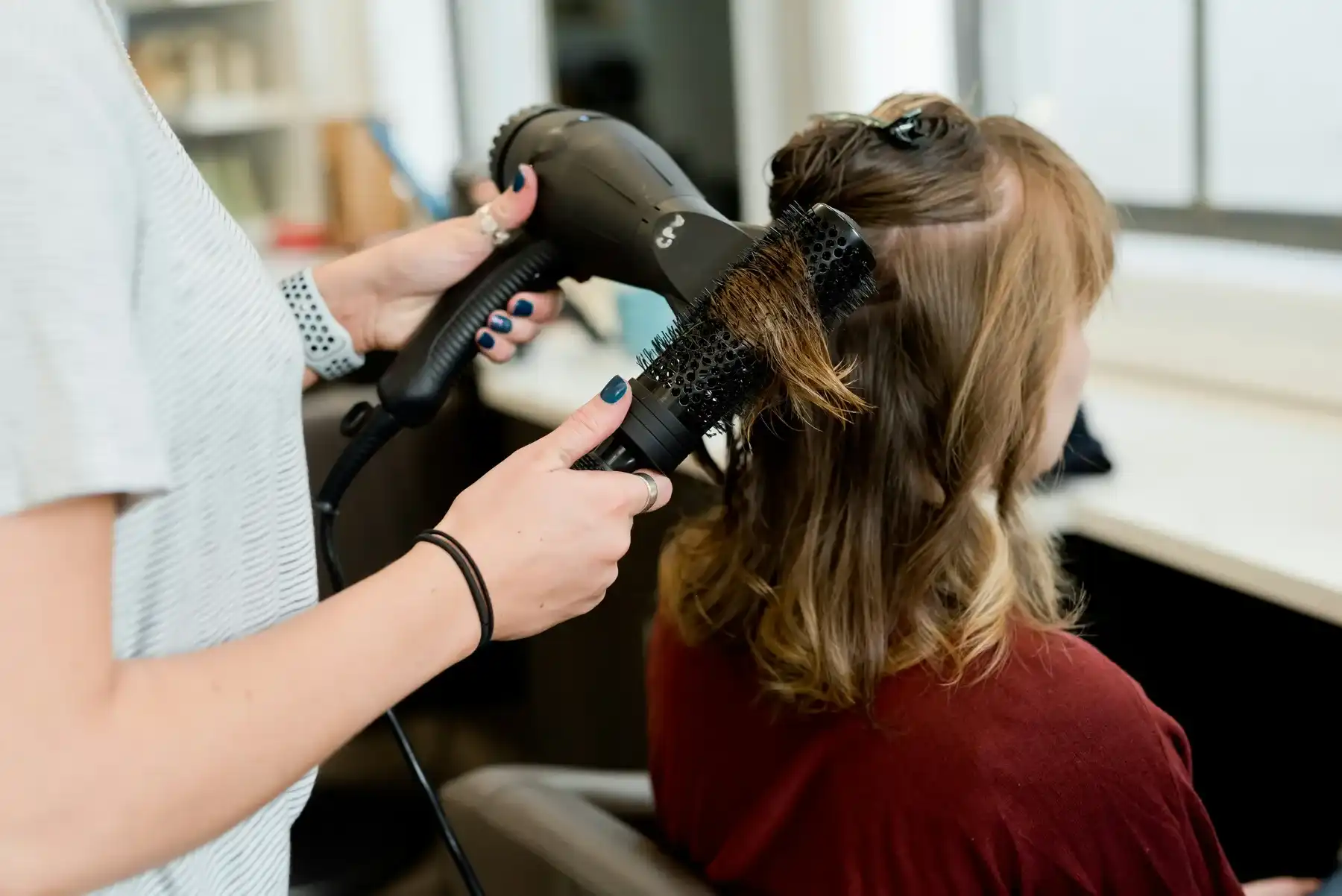 Une professionnelle réalise un coiffage avec une brosse et un sèche-cheveux